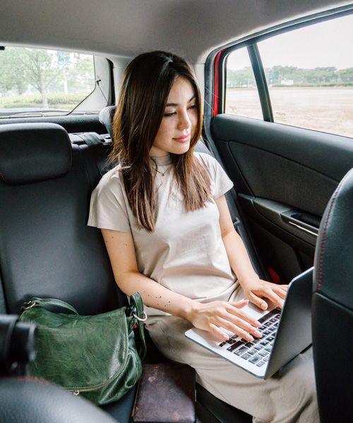 woman sitting in the back of a car working on a laptop